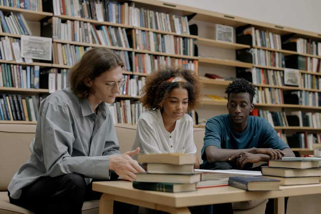 Two young men and a young lady between them are studying together inside a library Two young men and a young lady between them are studying together inside a library