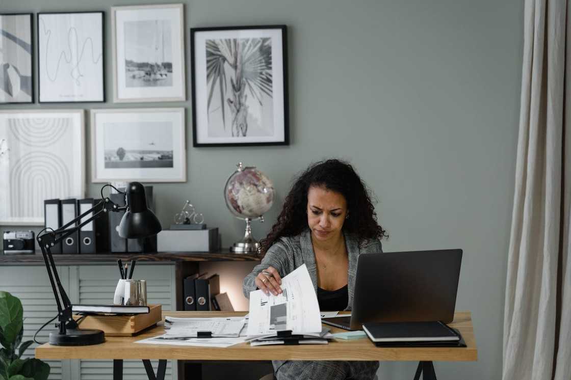 A woman reviewing paperwork beside a laptop.