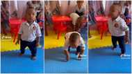 Baby wearing diaper sings in class filled with older children, moves funny as he touches his toes in video